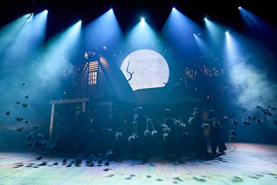 My Neighbour Totoro stage show – A shack with orange glow from windows stands in front of a projected moon surrounded by hase