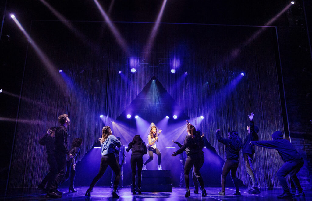 Singer surrounded by dancers lit in purple and blue spotlights.
