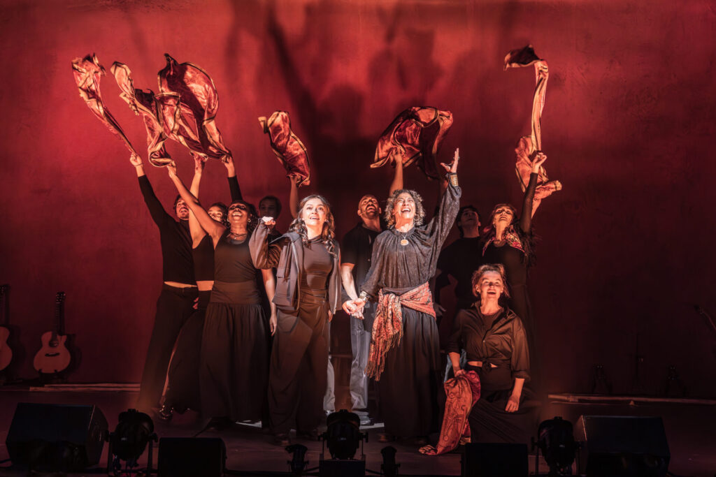 Elation sol blinder washes cast who stand with raised arms in fiery reds.